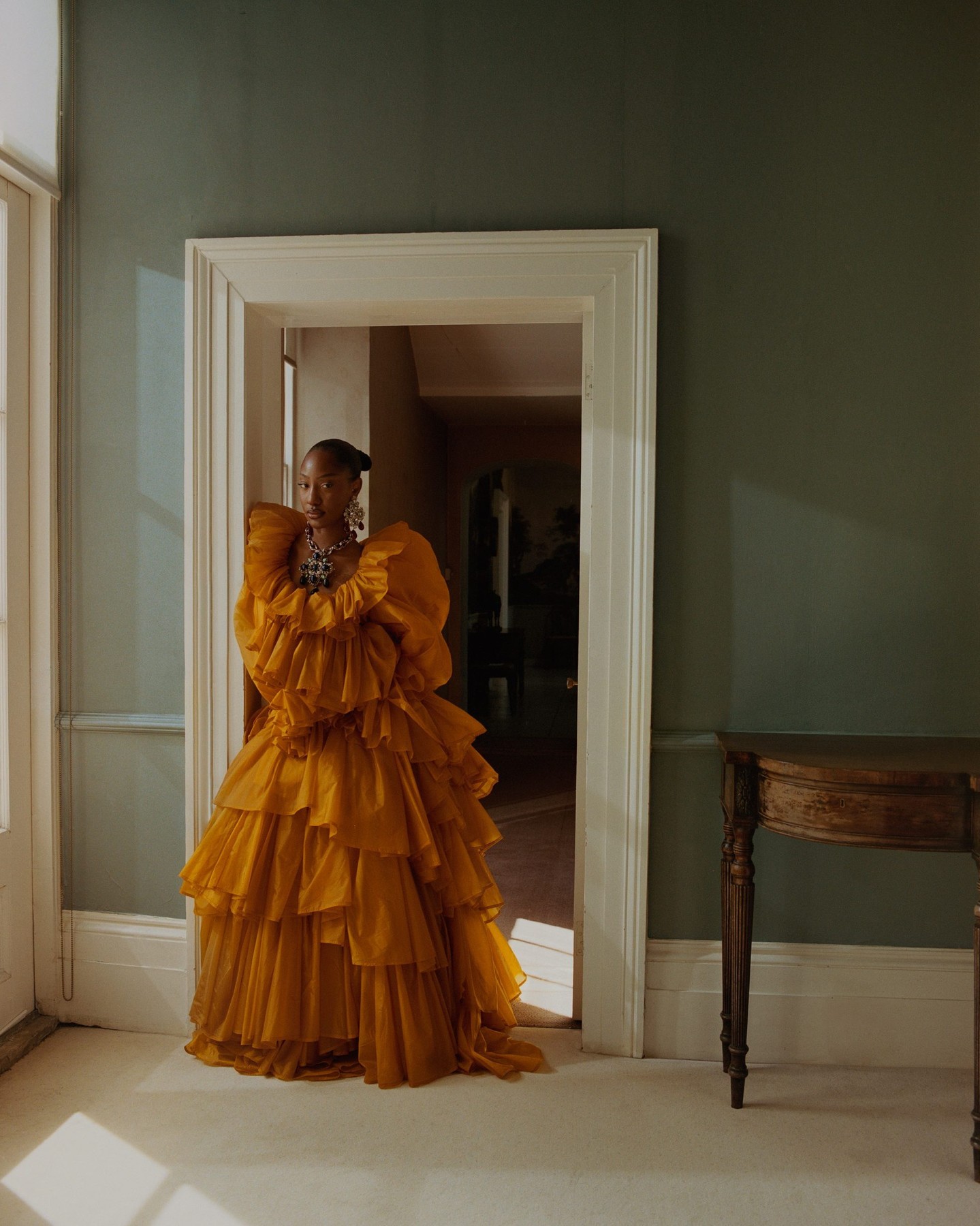 Tems wearing a mustard-yellow ruffled tiered dress by Saint Laurent with an ornate chandelier earring and a heavy statement pendant necklace.