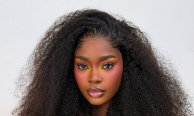 Dede Ashiogwu wears dark brown lip liner with nude-pink lipstick and clear gloss framed by long curly hair.