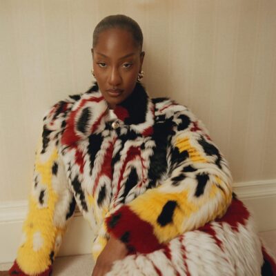 Tems wearing a patterned black, white, red, and yellow Chanel patchwork lambskin coat with gold LO Collections x Alex & Trahanas hoop earrings.