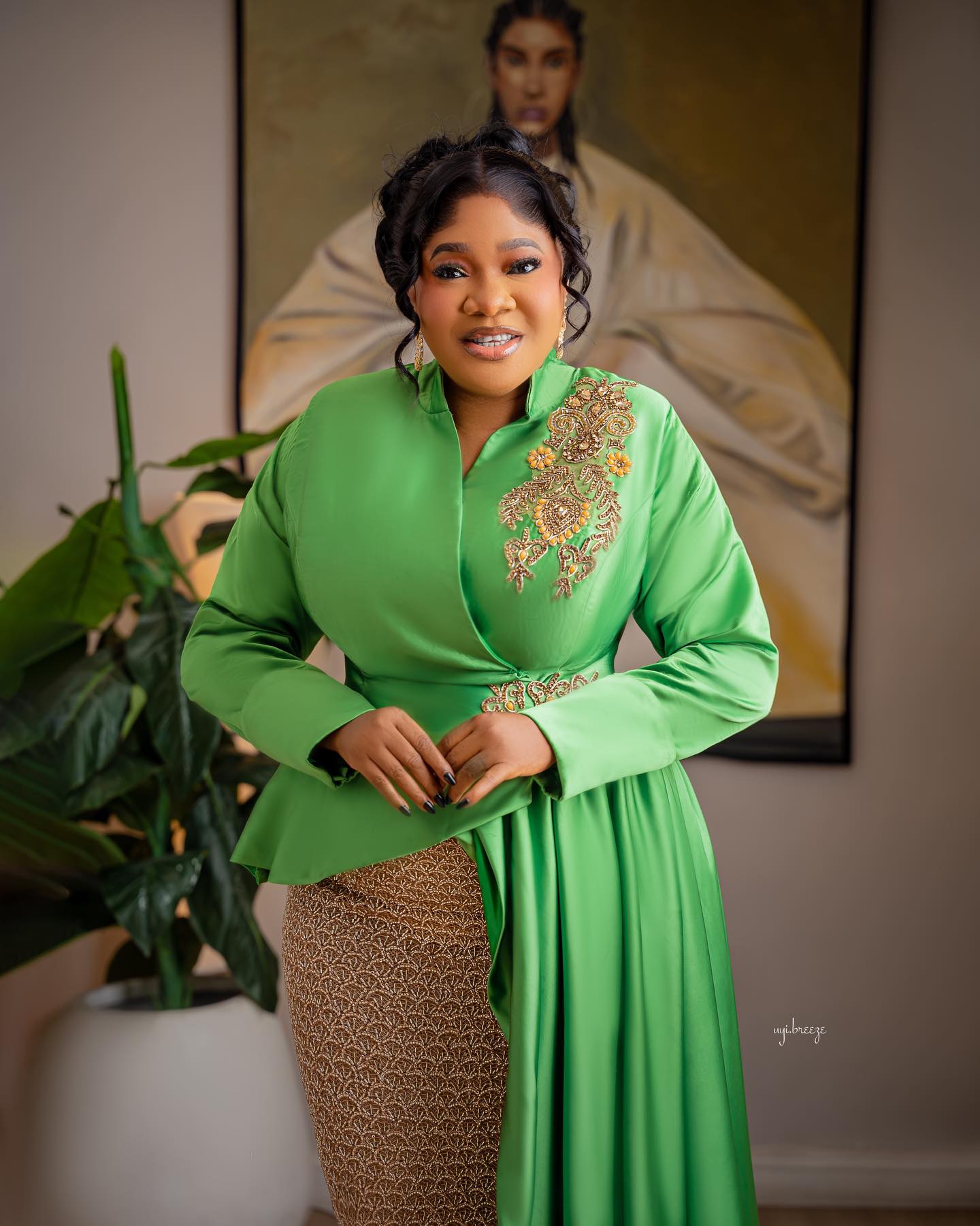 Toyin Abraham Ajeyemi in an apple-green satin peplum jacket blouse paired with a textured gold and bronze geometric pattern column skirt.
