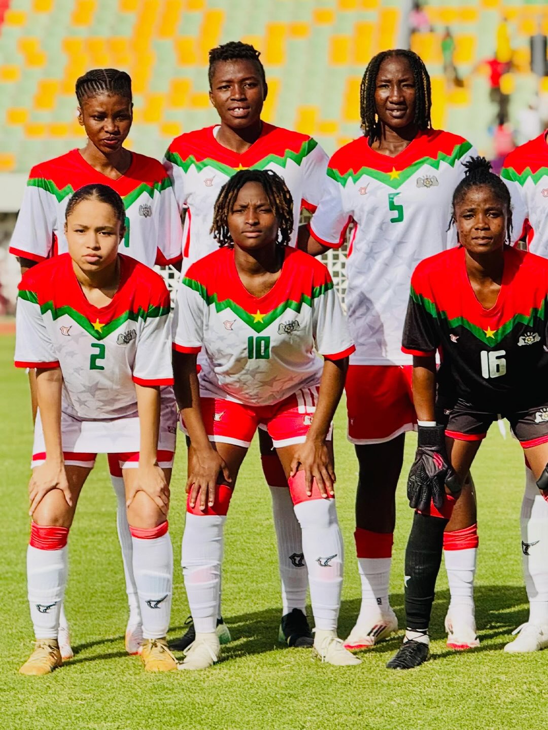 Burkina Faso women's national football team posing on the pitch in their white, red, and green match day kits.
