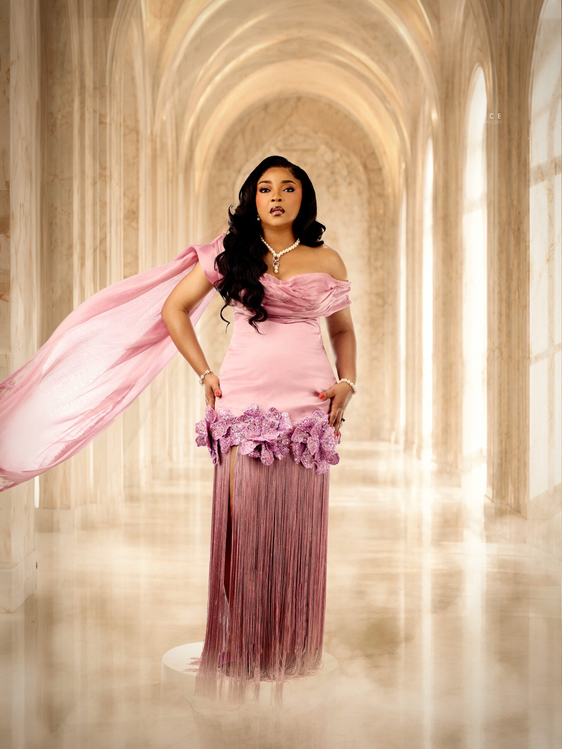 Linda Ejiofor-Suleiman looking over her shoulder in a pink off-the-shoulder gown with cascading floor-length fringe and a moving sash.