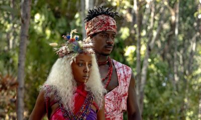 Thuso Mbedu as Zélie Adebola with white hair and a floral headpiece standing beside Damson Idris as Prince Inan in an Orïsha forest.