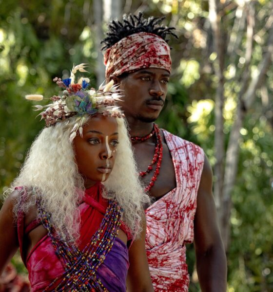 Thuso Mbedu as Zélie Adebola with white hair and a floral headpiece standing beside Damson Idris as Prince Inan in an Orïsha forest.