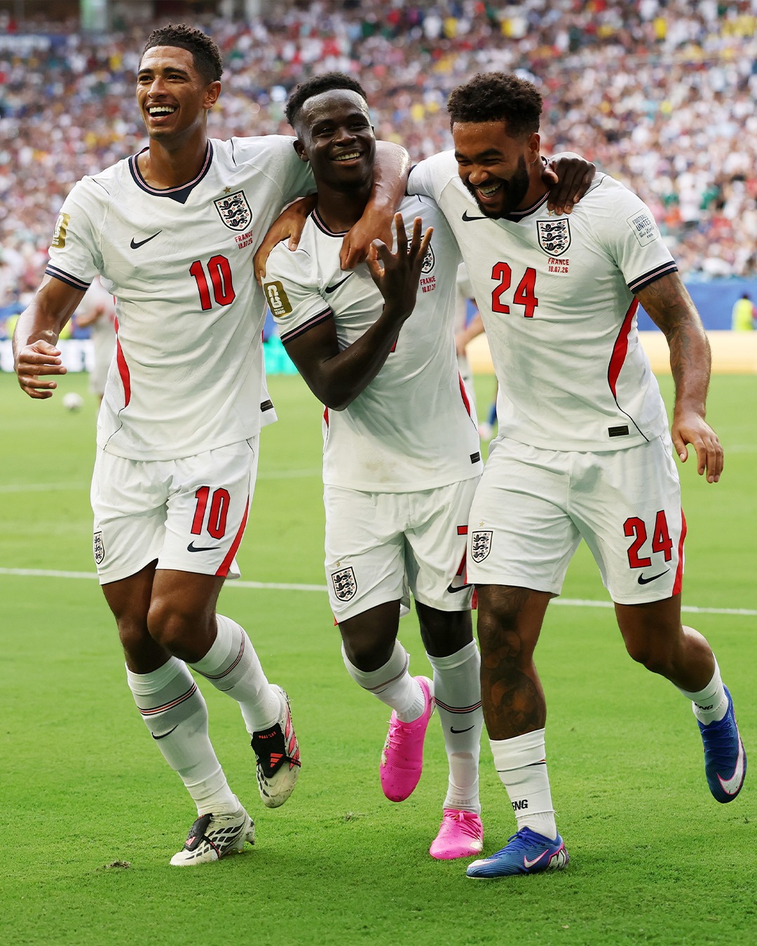England football players Jude Bellingham, Bukayo Saka, and Reece James smile and embrace on the pitch during the match against France.