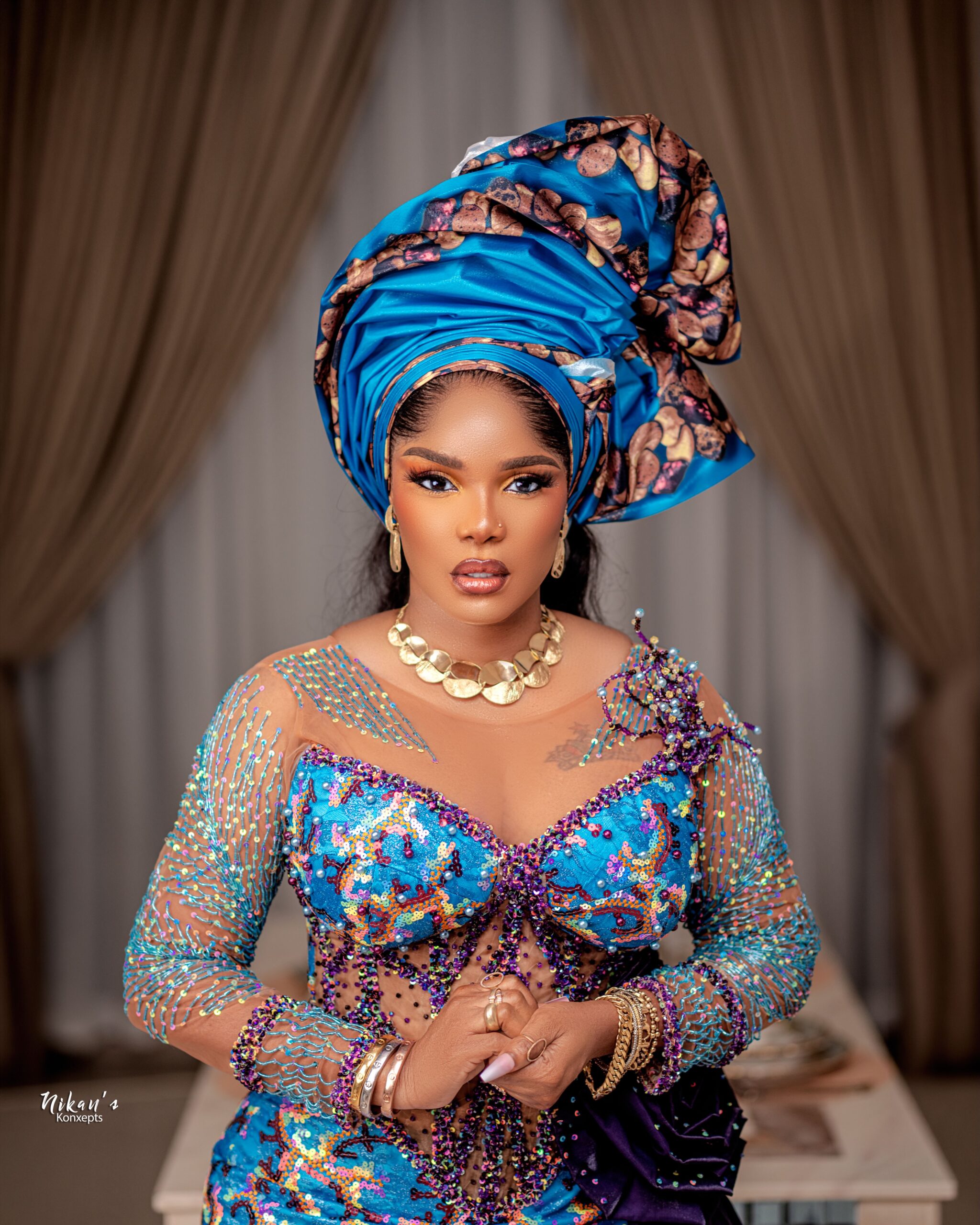 Iyabo Ojo in a detailed turquoise and purple illusion corset gown, showcasing the structured metallic gele and gold choker necklace.