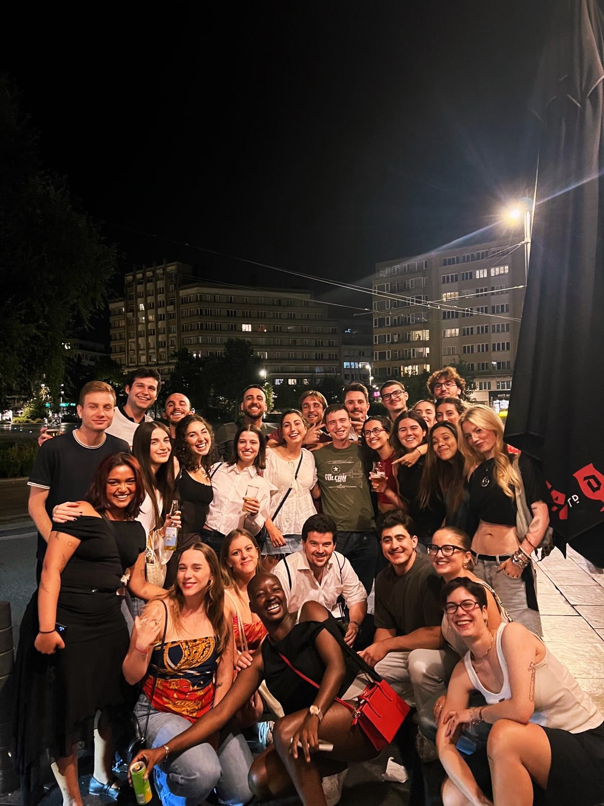 Saskay sits smiling with her Master in Global Security and Strategy classmates during a celebratory night out on a city street in Brussels.