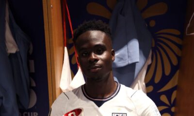 Bukayo Saka in the stadium dressing room holding the official Man of the Match trophy and the signed match ball.