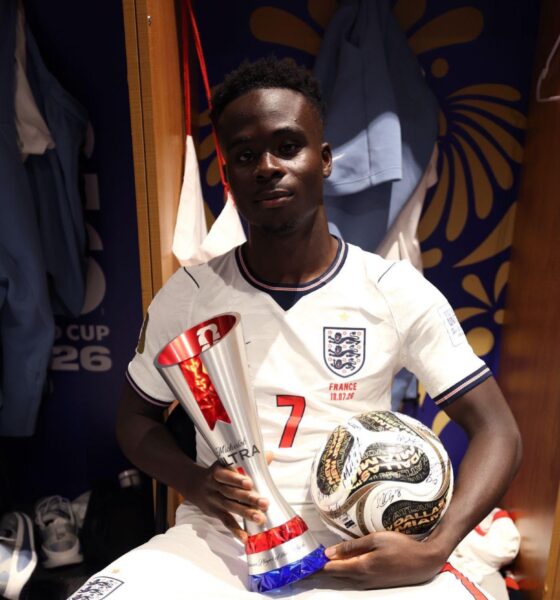 Bukayo Saka in the stadium dressing room holding the official Man of the Match trophy and the signed match ball.