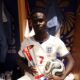 Bukayo Saka in the stadium dressing room holding the official Man of the Match trophy and the signed match ball.