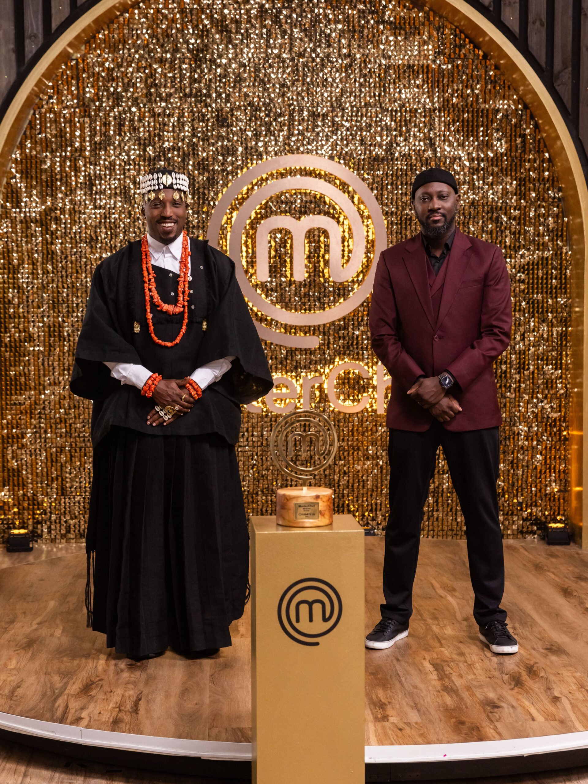 MasterChef Nigeria judges Chef Stone and Chef Eros standing beside the trophy on the grand finale stage.