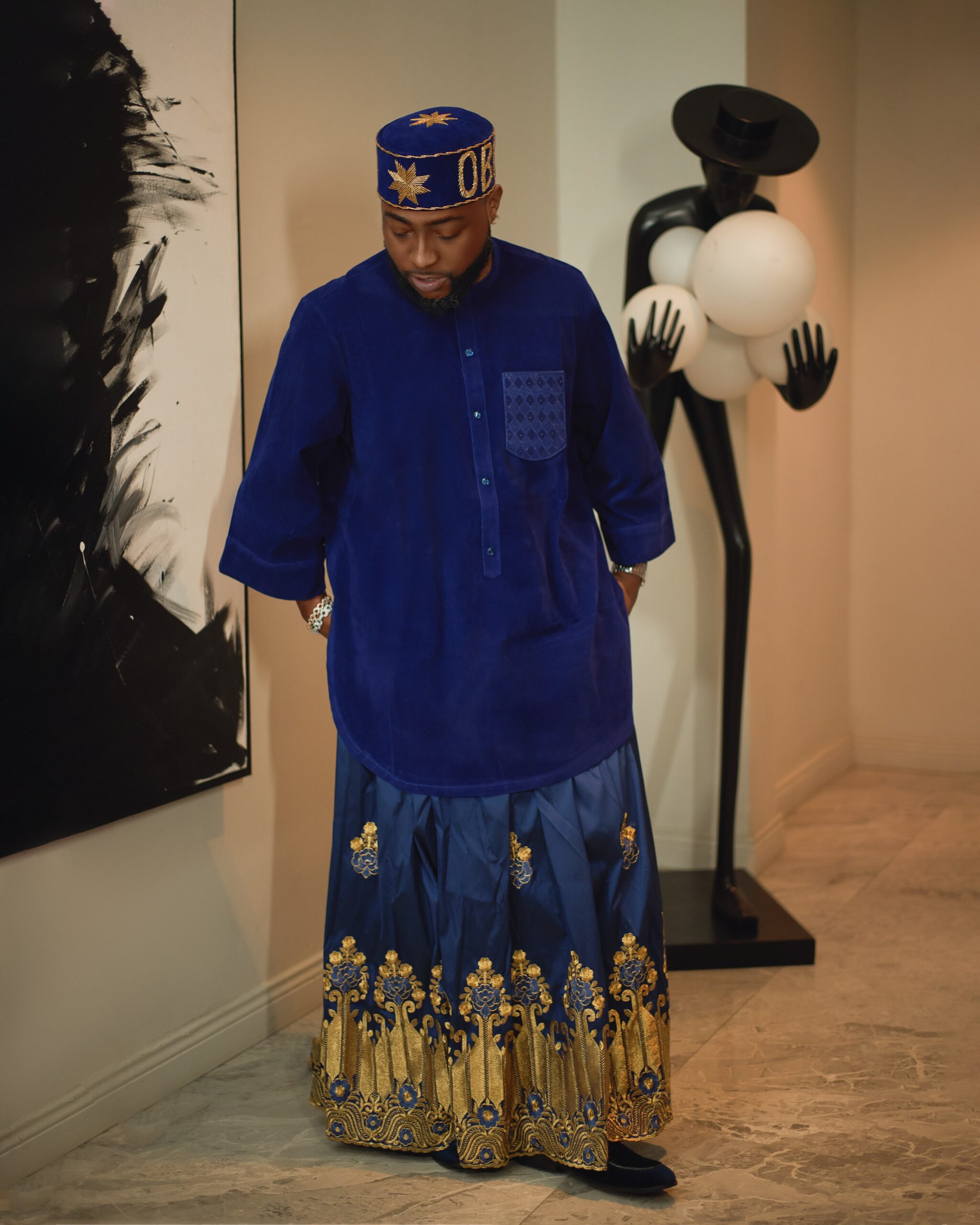 Davido showcasing a royal blue velvet three-quarter sleeve tunic with a geometric stitched chest pocket, silver wrist watch, and gold OBO cap.