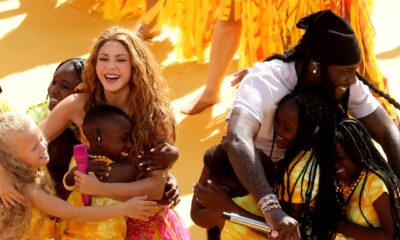 Burna Boy and Shakira embrace members of the Ghetto Kids in a group hug on the yellow stage following their halftime show performance.