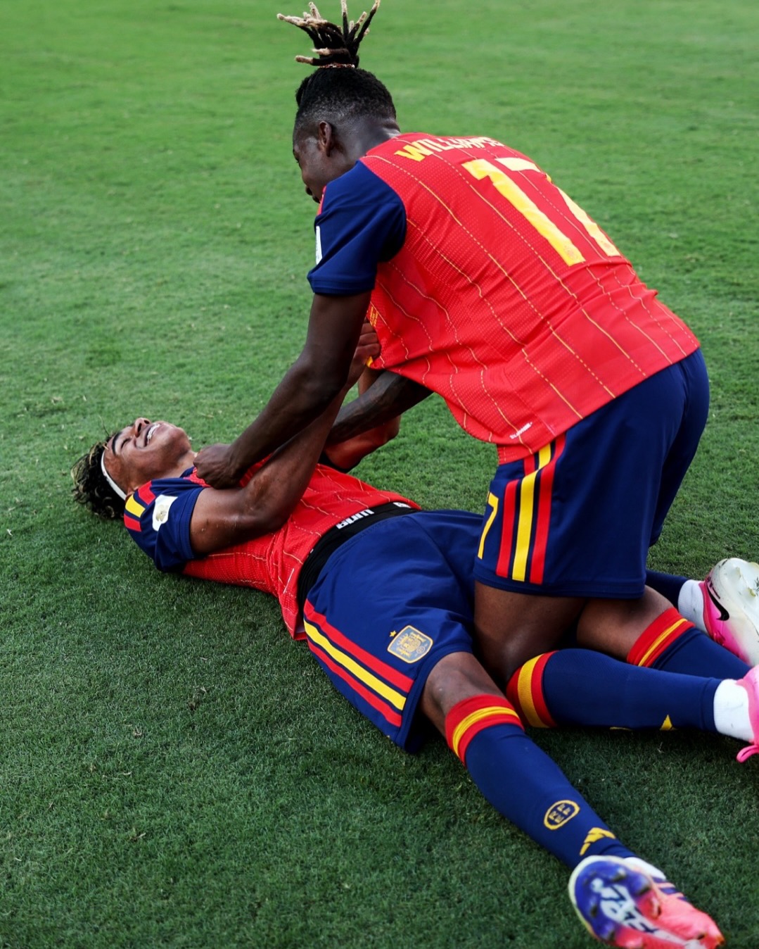 Nico Williams kneels over teammate Lamine Yamal lying on the pitch celebrating Spain's World Cup final win.