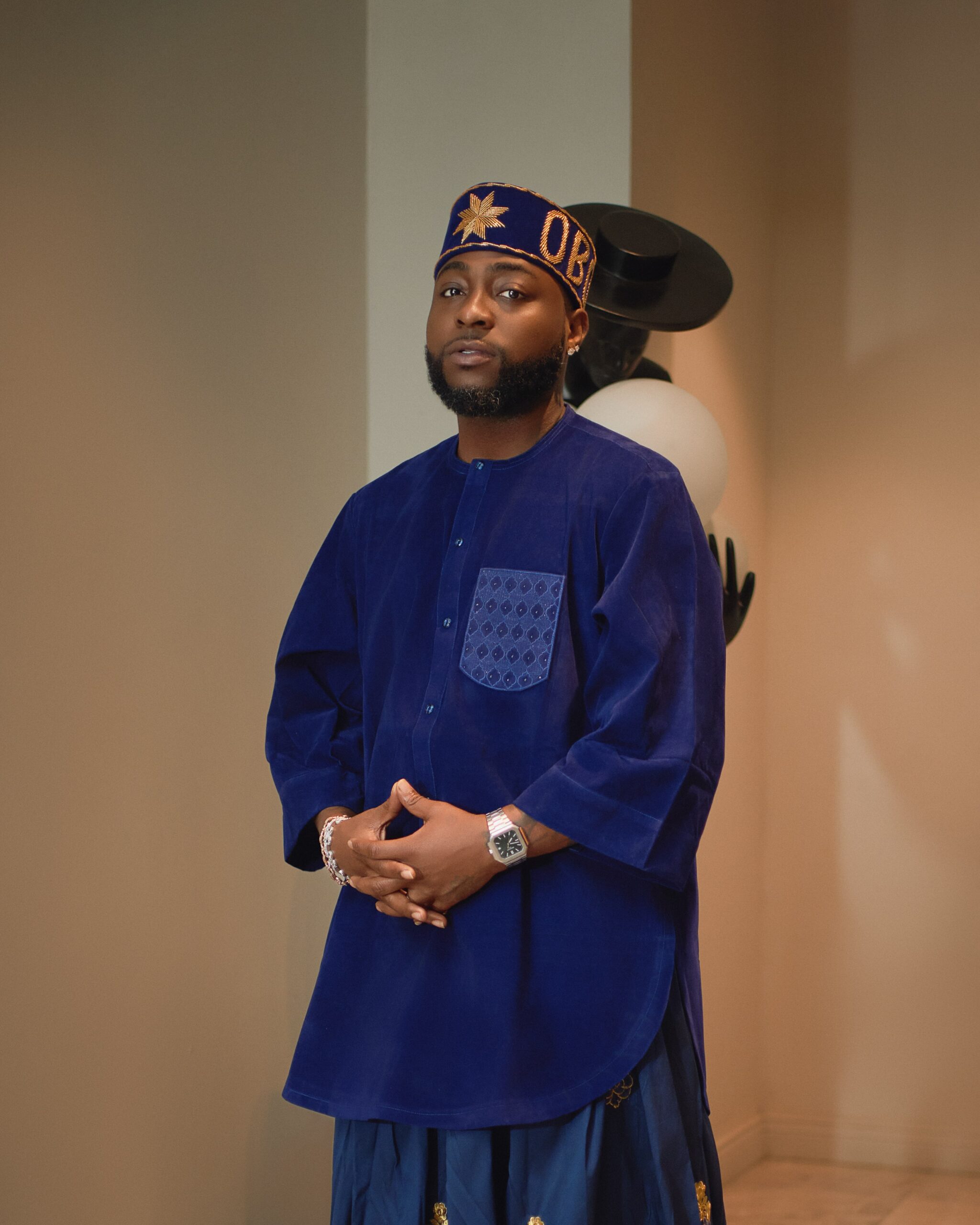 Davido wearing a royal blue velvet tunic, gold embroidered silk wrapper, and customised OBO velvet cap for a traditional Nigerian event.