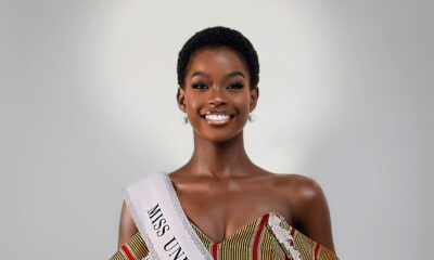 Kimberly Jael Aremo Acio wearing the official Miss Universe Kole sash over a white lace-embellished gown with an off-the-shoulder striped corset top for her official pageant delegate portrait.