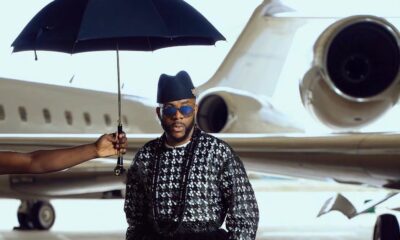 Ebuka Obi-Uchendu in a long-sleeved lattice sequin tunic and floor-length black velvet wrapper skirt paired with zebra-print leather loafers inside an aviation hangar for Big Brother Naija Season 11.