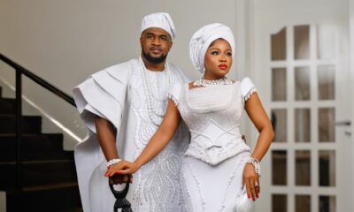 Femi Atere resting his hand on a carved lion cane alongside Veekee James wearing a pearl-beaded white gown and white gele.