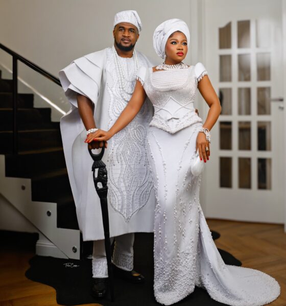 Femi Atere resting his hand on a carved lion cane alongside Veekee James wearing a pearl-beaded white gown and white gele.