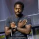 David Jonsson crossing his arms over his chest in the Wakanda Forever salute while holding a microphone on stage at San Diego Comic-Con 2026.