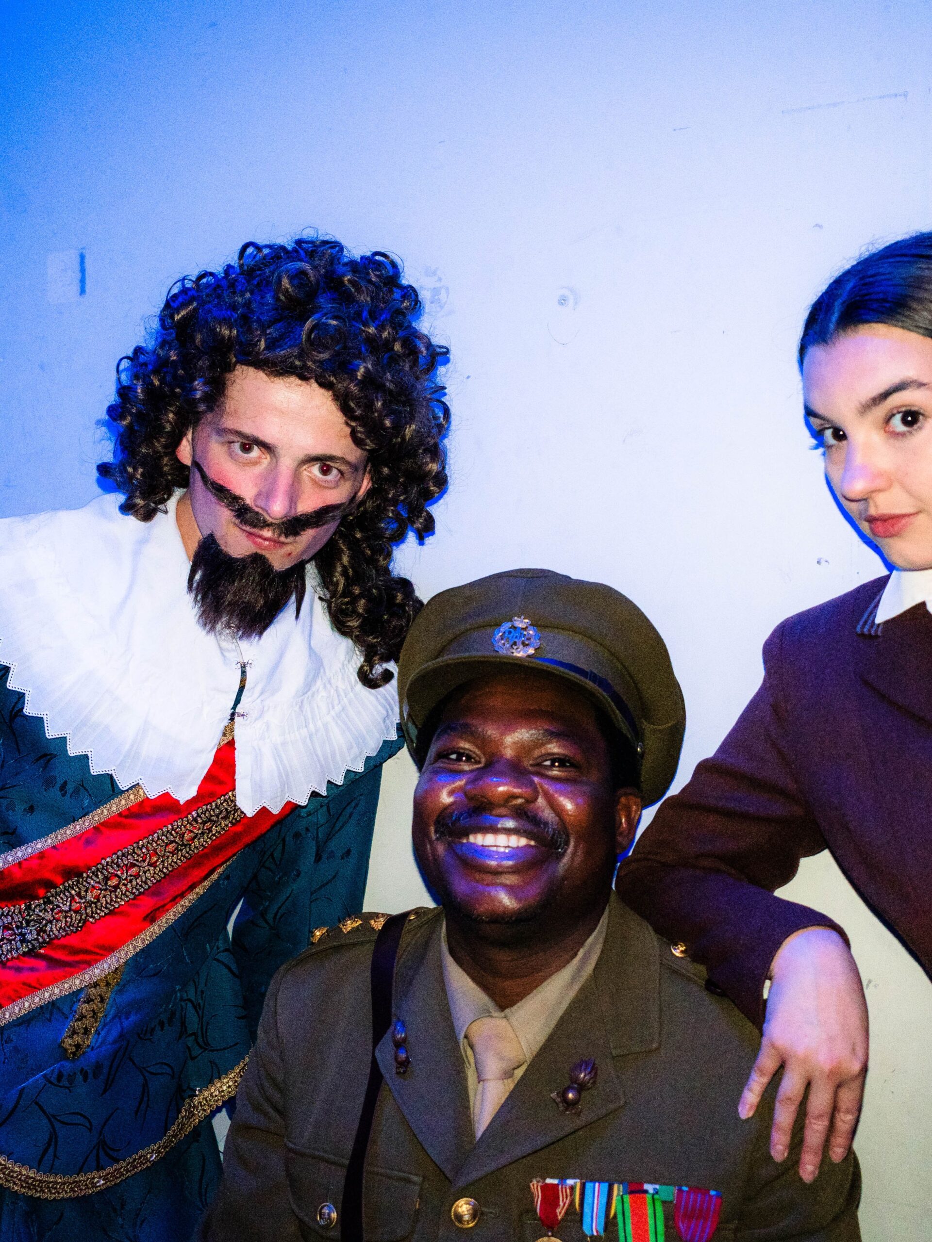 Debo Adedayo smiling in military costume alongside cast members in period wigs and 17th-century costumes backstage at Mountview Academy of Theatre Arts.