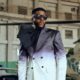 Ebuka Obi-Uchendu in a double-breasted ATAFO jacket transitioning from charcoal black to off-white, styled with a sculptural black lapel bow, peak lapels, and square sunglasses at the Big Brother Naija Season 11 launch.