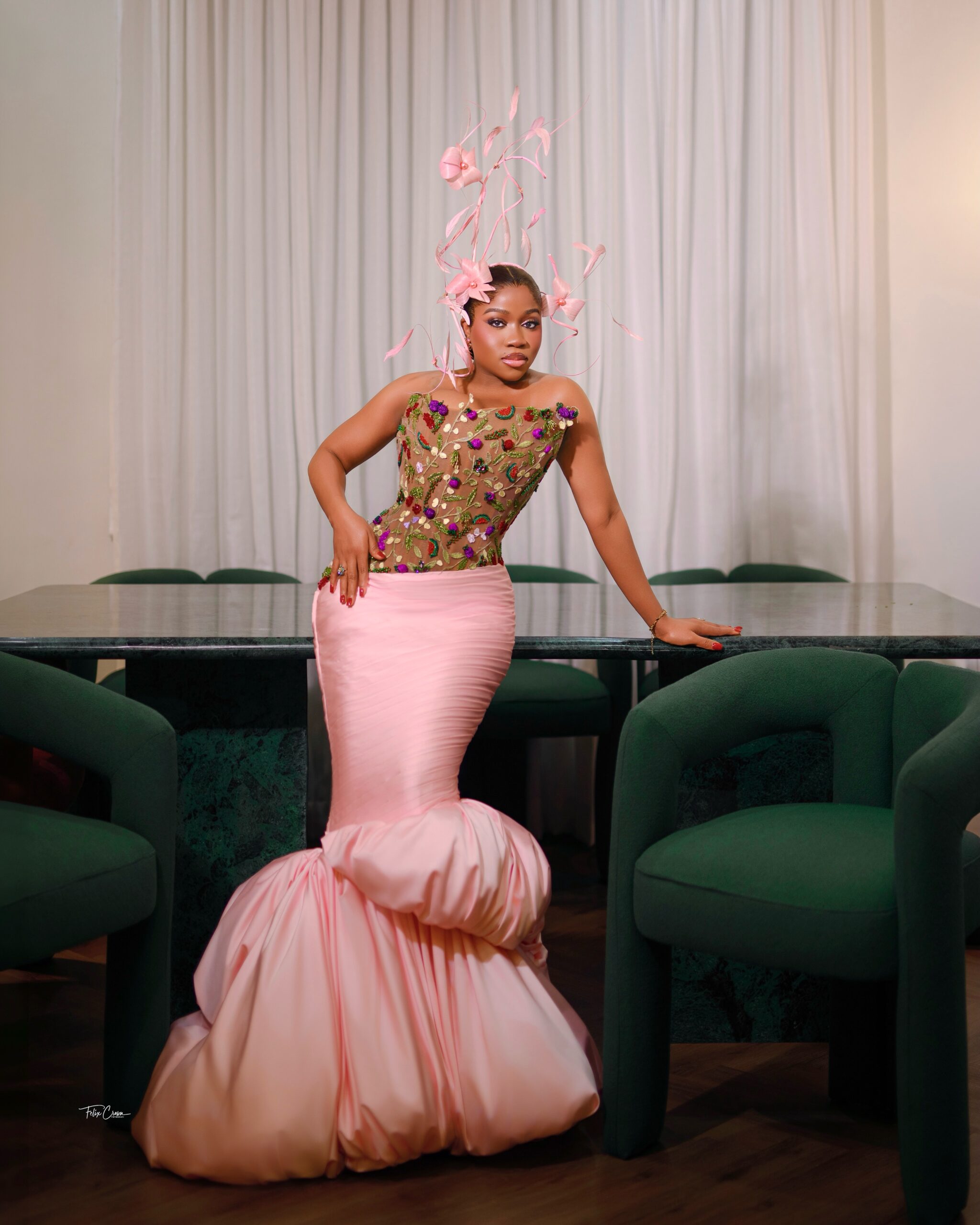 Fashion designer Veekee James posing in a strapless pink mermaid dress by her own brand with sheer floral corset and sculptural feather fascinator at baby Eliana's reception