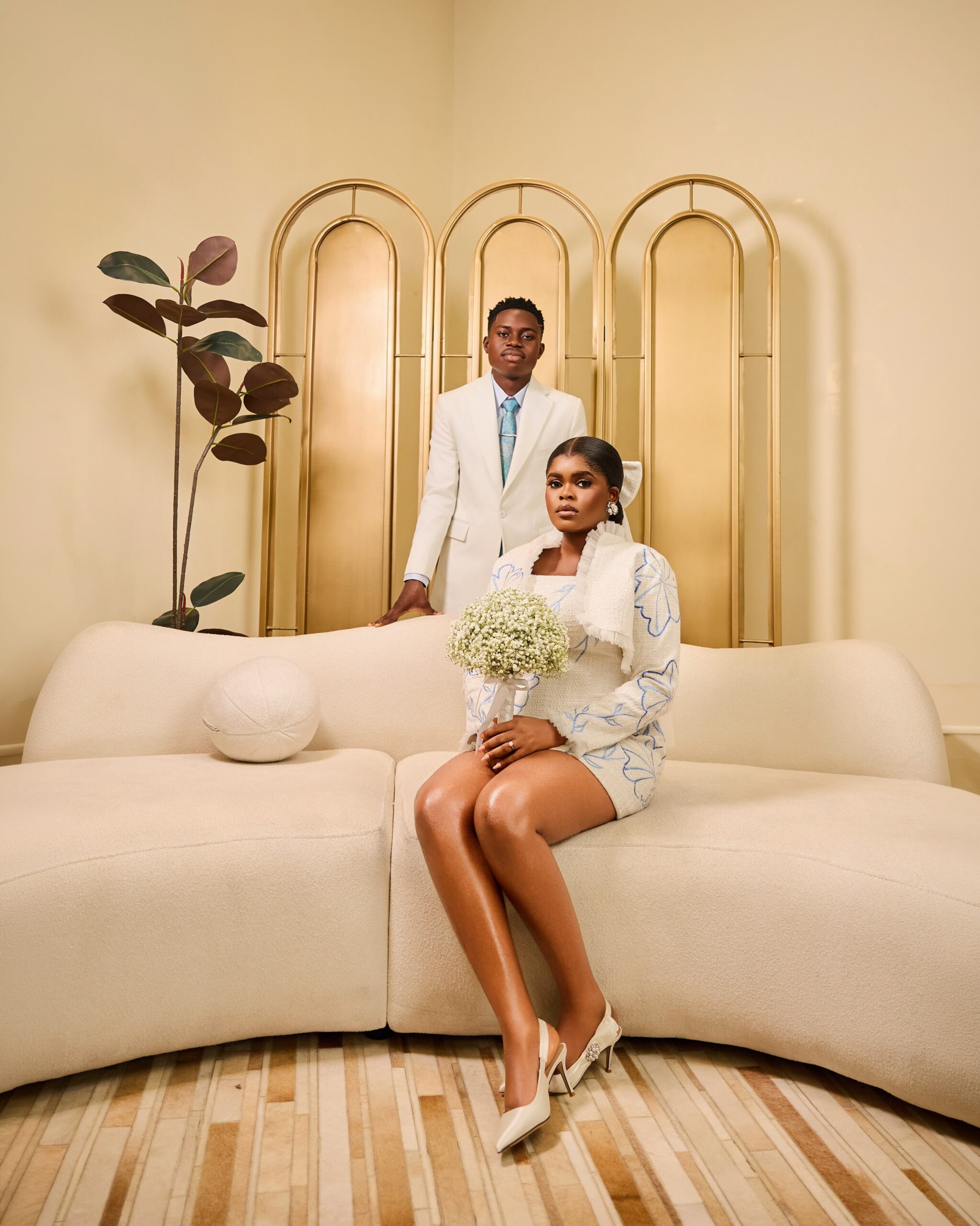 Jarvis in a Prudential blue floral embroidered tweed mini dress seated beside Peller in an off-white suit.