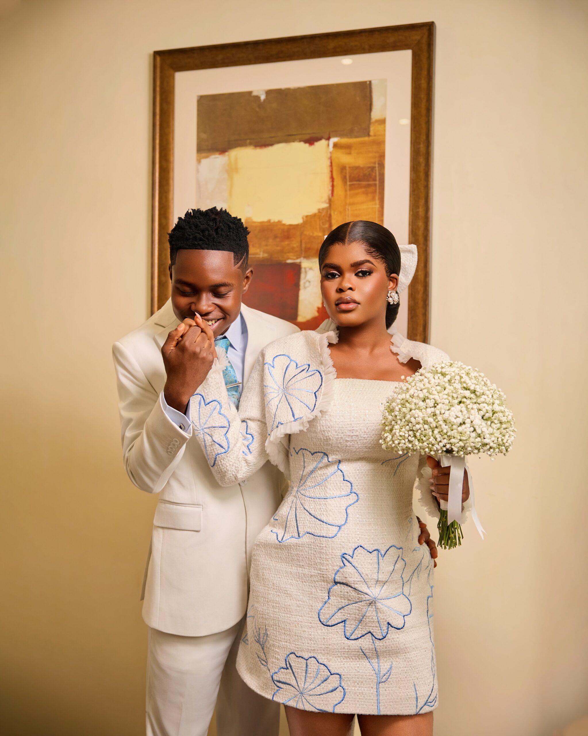 Peller kissing Jarvis hand while wearing an off-white suit beside Jarvis holding a baby's breath bouquet.