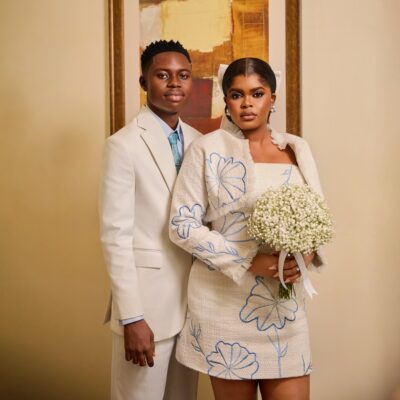 Studio portrait of Peller and Jarvis in off-white wedding outfits with blue floral embroidery.