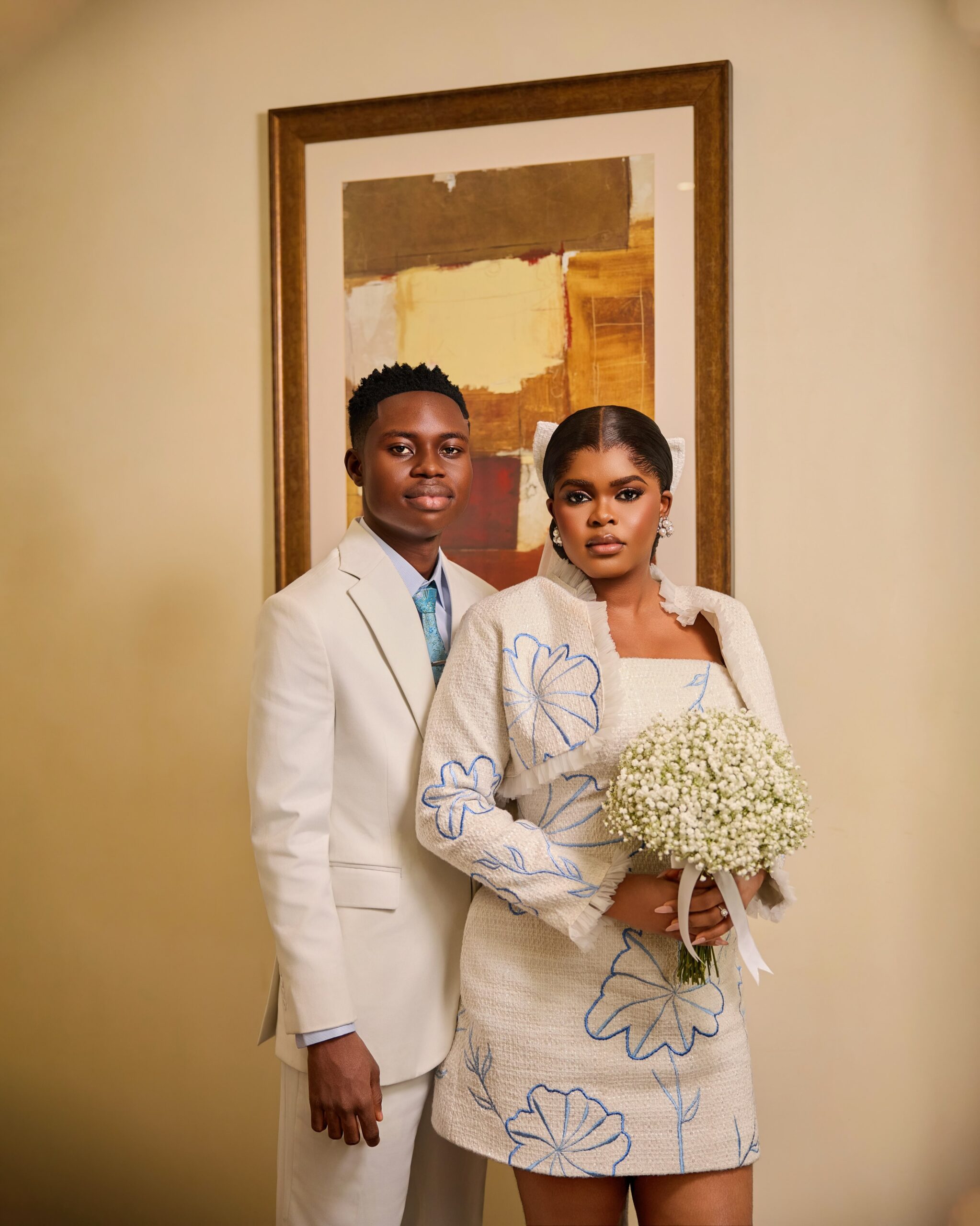 Studio portrait of Peller and Jarvis in off-white wedding outfits with blue floral embroidery.