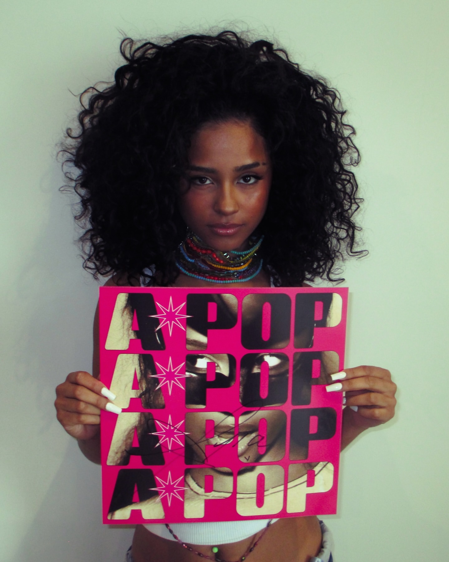 Tyla holding an autographed neon pink A*POP album vinyl insert promoting her sophomore album.