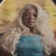 Nigerian singer Fave wearing a blue textured top, silver necklace, and nose rings, with platinum blonde hair, rhinestones above her eyebrows, and pink eye makeup in the official Dance music video from her RnBling EP.