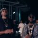 Houston-born singer NO11 in a black tee and beanie standing next to Davido who is wearing a striped shirt, sunglasses, and layered gold chains in the Gimme Dat Ting music video.