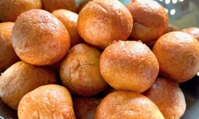Freshly fried, golden brown, perfectly round Nigerian puff-puff balls in a colander.