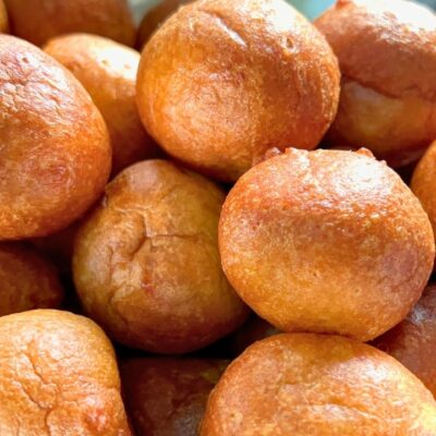 Freshly fried, golden brown, perfectly round Nigerian puff-puff balls in a colander.