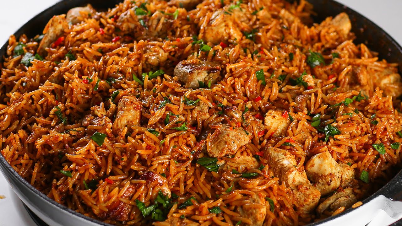 A large black skillet filled with freshly cooked butter chicken rice garnished with chopped green herbs.