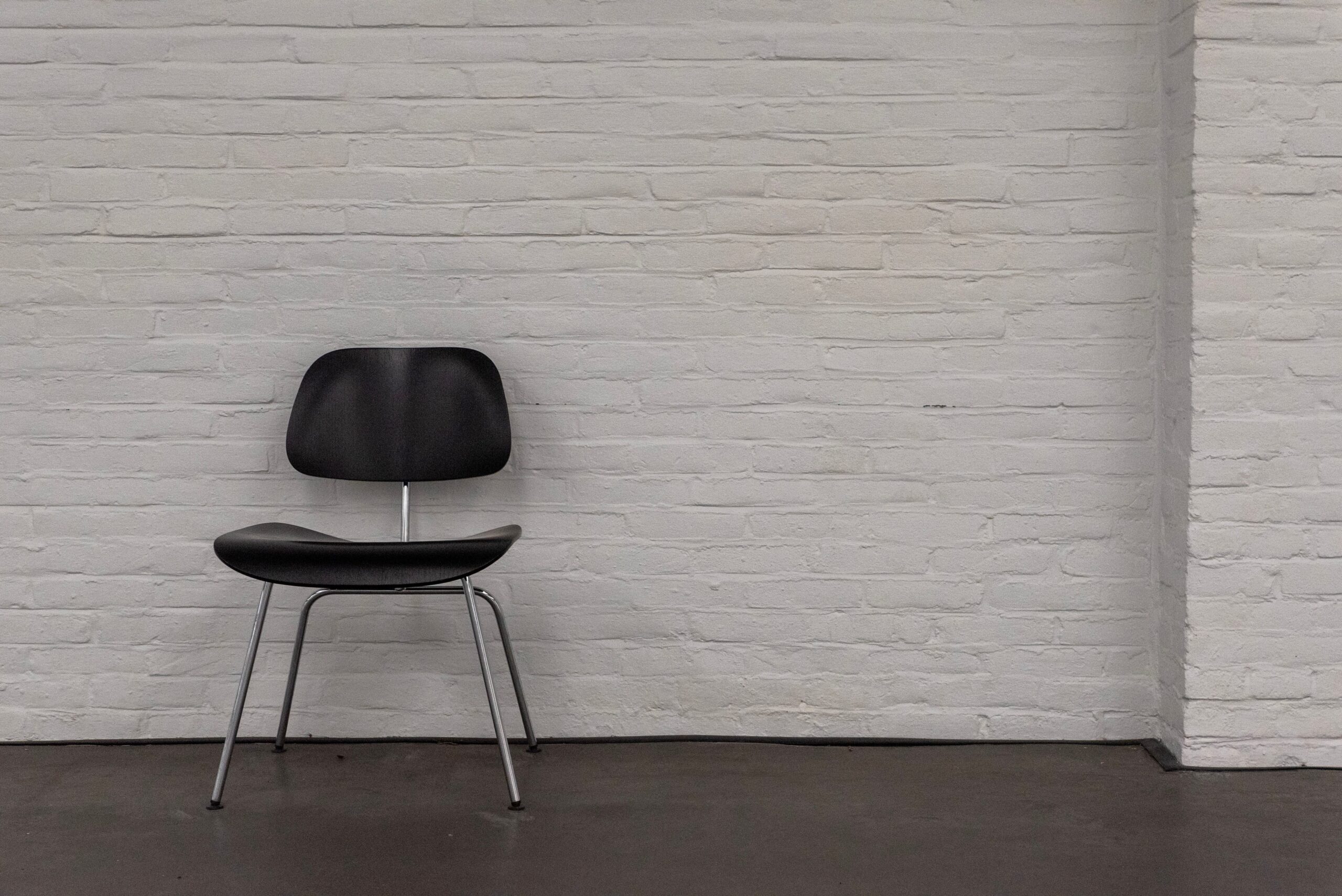 A sleek black chair stands against a textured white brick wall in an empty room. Photo credit: Jan van der Wolf/Pexels