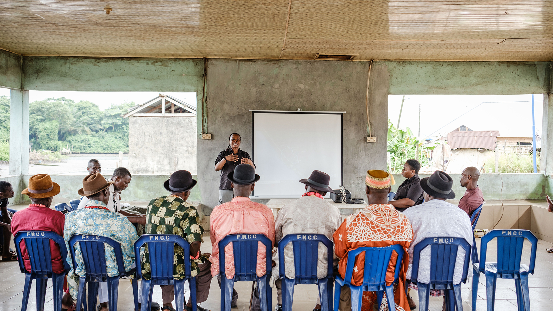 Rachel Ikemeh conducting a conservation training session in front of a projection screen for seated Niger Delta community elders and residents.