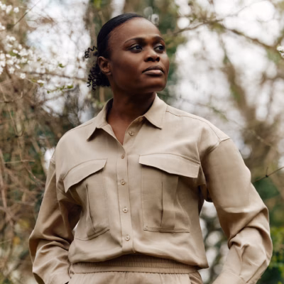 Nigerian biologist Rachel Ikemeh in a beige utility shirt and a Rolex watch, looking onward against a backdrop of forest foliage.