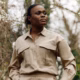 Nigerian biologist Rachel Ikemeh in a beige utility shirt and a Rolex watch, looking onward against a backdrop of forest foliage.