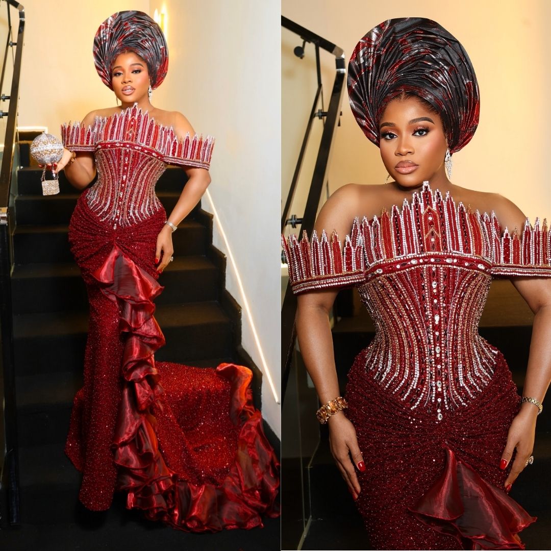 Veekee James wearing a rich crimson corset gown with geometric spires along the off-the-shoulder neckline, a ruffled side train, and a crystal sphere clutch at Peller and Jarvis' traditional wedding.