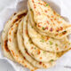 Freshly baked homemade skillet naan brushed with melted garlic butter and chopped parsley in a parchment-lined basket.
