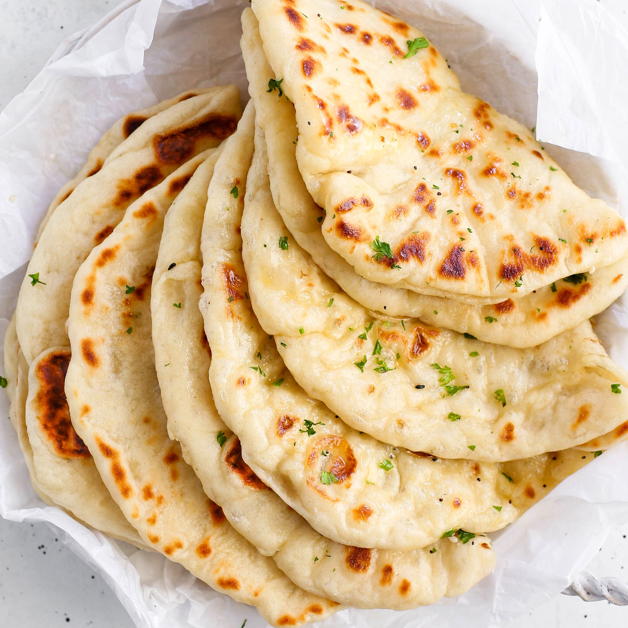 Freshly baked homemade skillet naan brushed with melted garlic butter and chopped parsley in a parchment-lined basket.