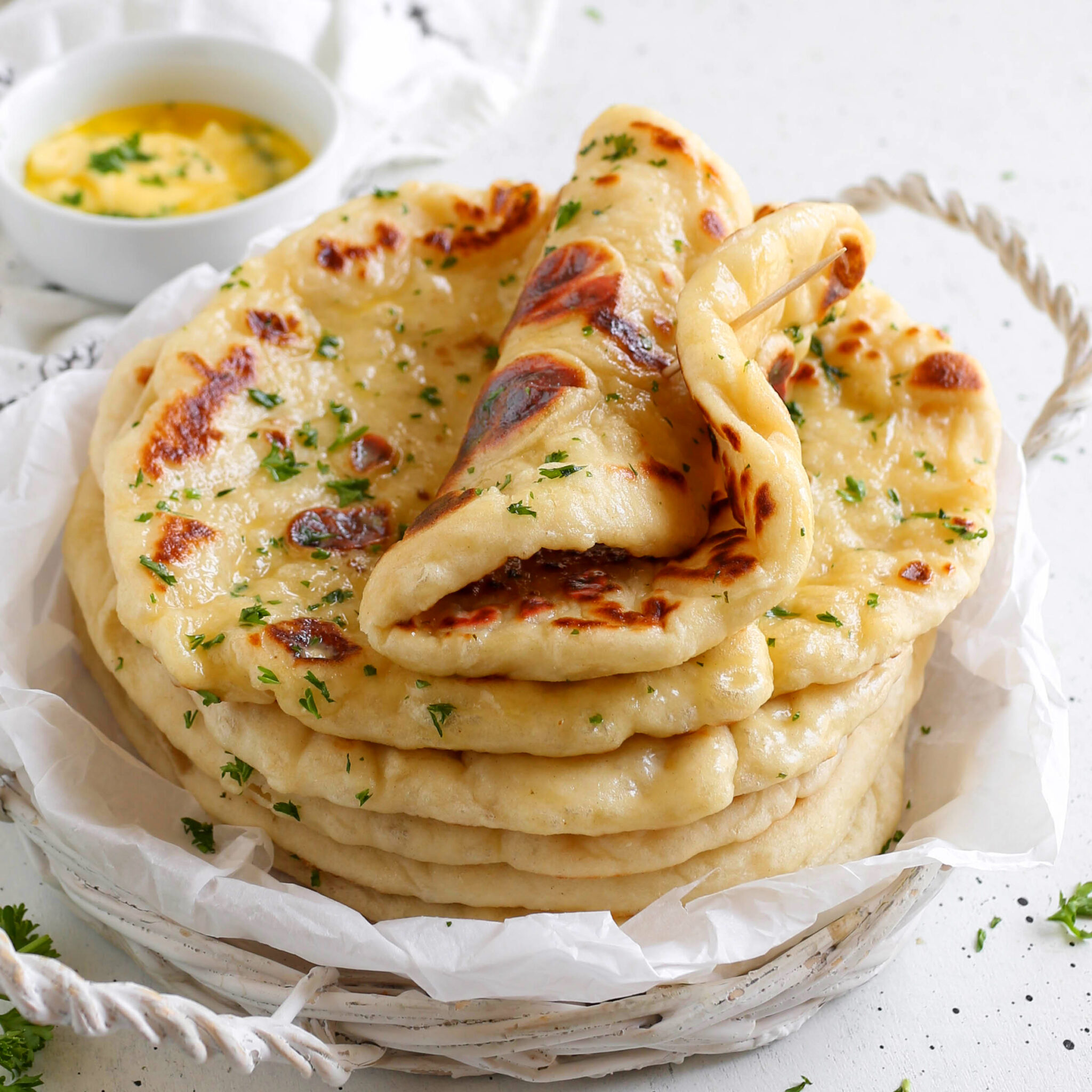 Stack of warm garlic butter naan flatbreads with one piece folded over, served alongside a small bowl of melted butter dipping sauce.