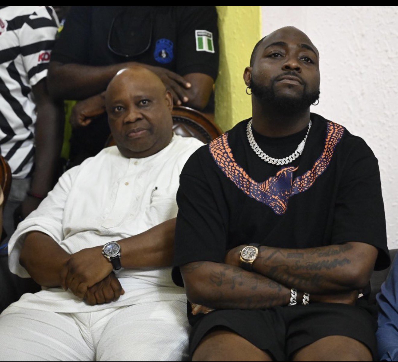 Osun State Governor Ademola Adeleke wearing a white traditional outfit sitting next to his nephew, musician Davido, dressed in a black t-shirt and silver chain.