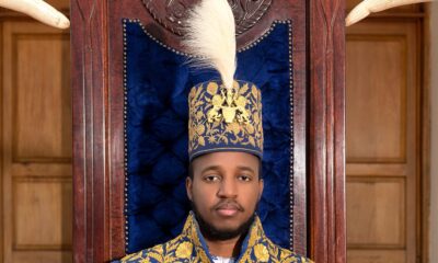 King Oyo Nyimba Kabamba Iguru Rukidi IV seated on the Tooro Kingdom throne in embroidered blue ceremonial robes and a royal feather crown.