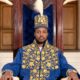 King Oyo Nyimba Kabamba Iguru Rukidi IV seated on the Tooro Kingdom throne in embroidered blue ceremonial robes and a royal feather crown.