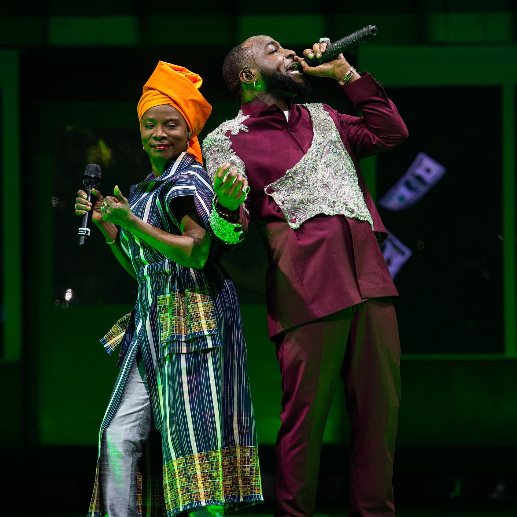 Angélique Kidjo in a striped outfit and orange headwrap performing live on stage alongside Nigerian music star Davido at The O2 Arena in London in 2024.