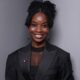 Nigerian filmmaker and writer Uzoamaka Power smiling in a black suit jacket and braided updo hairstyles, director of the short film Siraam.